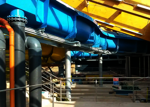 Blauer Wildwasserfluss führt durch den Innenbereich eines Erlebnisbads mit sichtbarer Technik.