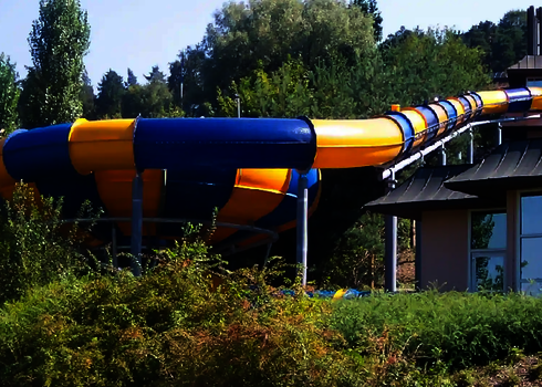 Blick von der Seite auf eine Wasserrutsche in grüner Umgebung, gelegen an einem Haus.