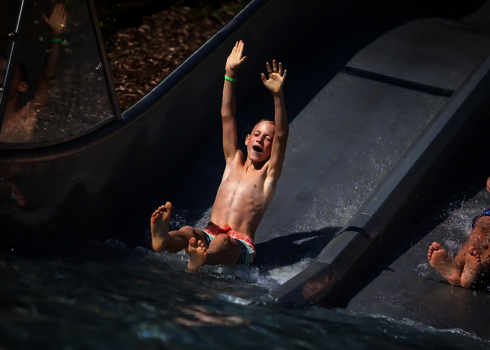 Zwei Jungs rutschen lachend nebeneinander die Trio-Slide hinunter ins Wasser.