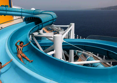 Kinder rutschen lachend die blaue 2-in-1 Racer Wasserrutsche auf einem Kreuzfahrtschiff hinunter.