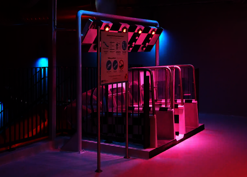 Leerer Startbereich zweier Rutschen mit Sensorampfel und Hinweisschildern, rosa Licht.