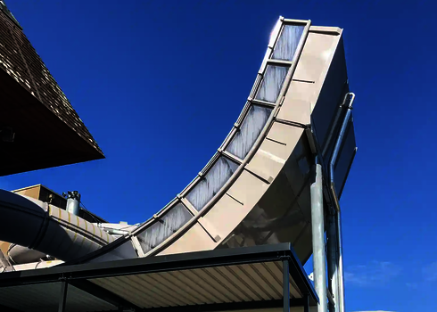Outdoor-Ansicht der Boomerang-Rutsche mit transluzenter Verkleidung unter blauem Himmel.