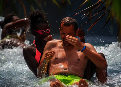 Ein Mann und zwei Kinder rutschen gemeinsam lachend durch den Wildwasserfluss.