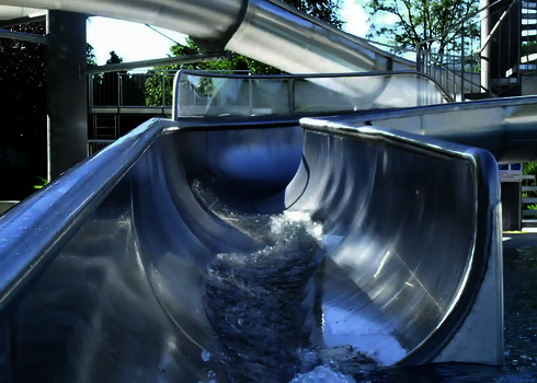 Wasser strömt durch eine halboffene Edelstahlrutsche mit Acrylglas-Seitenwand.