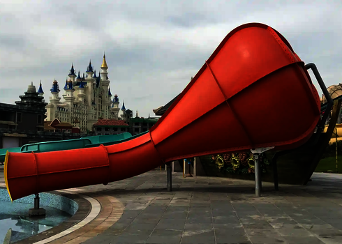Ein roter Crazy Cone endet in einem flachen Wasserbecken, im Hintergrund ein Schlossgebäude.