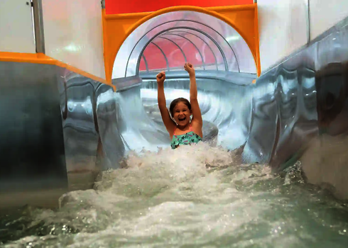 Ein Mädchen rutscht lachend aus einer WR1040 Wasserrutsche mit gläsernem Tunnel.