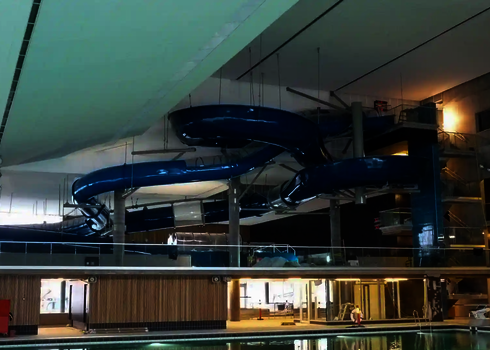 Ansicht eines Hallenbads, in dem eine große blaue RR1400 Reifenrutsche von der Decke hängt.