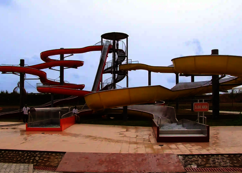 Eine rote Freifallrutsche aus Edelstahl, daneben ein gelber Crazy River mit Auslauf und Treppenturm in einem Wasserpark.
