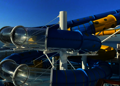 Geschwungene blau-gelbe RR900 Wasserrutsche mit transparenten Acryl-Abschnitten vor blauem Himmel.