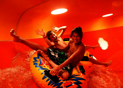 Zwei Kinder rutschen lachend auf gelbem Reifen durch die orangene Family Twister Wasserrutsche.