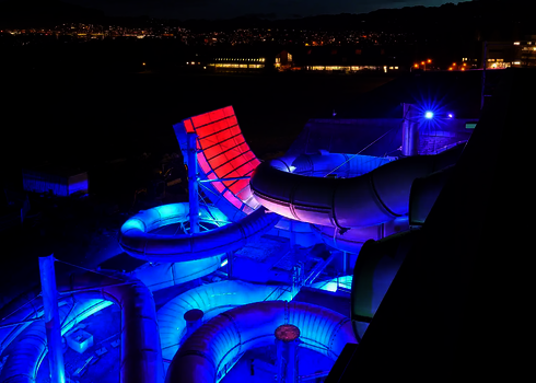 Große Wasserrutschenanlage mit bunten LED-Lichtern und Halfpipe bei Nacht.
