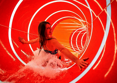 Eine rote Wasserrutsche von innen, mit einer rutschenden, lachenden Frau.