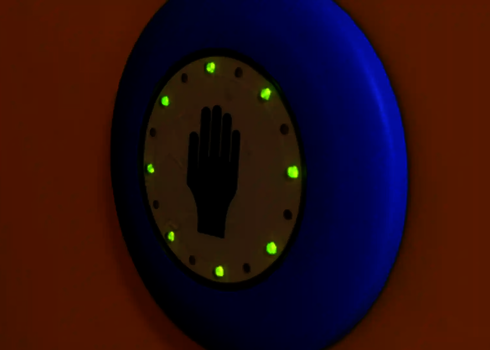 Grün leuchtender Auswahlknopf mit Hand-Symbol auf oranger Rutschenwand.