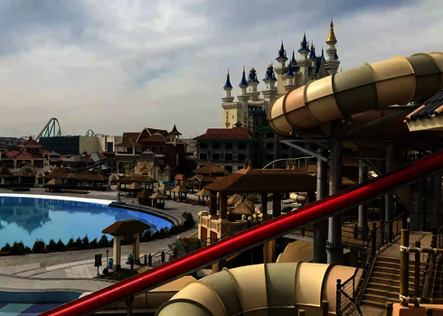 Large water park with castle backdrop and striking red slide channel next to a raft conveyor.