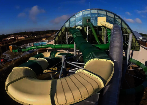 Blick auf ein Hallenbad, mit einem grün weißen Family Twister im Vordergrund und einem grünen Fallstart im Hintergrund.