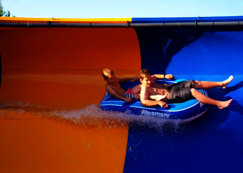 Zwei Kinder rutschen hintereinander sitzend in einem Reifen die Raft Bowl Rutsche entlang.