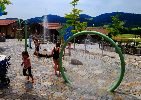 Kinderwasserbereich mit Wie-Spray Elementen vor bergiger Kulisse.