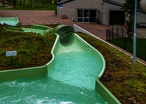Grüner Tunnelrutschenabschnitt des Wildwasserflusses mit Wegweiserschild daneben.