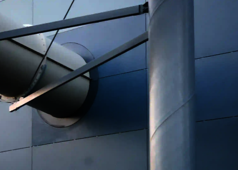 Wasserrutsche durchdringt blaugraue Metallfassade, mit sichtbaren Halterungen.