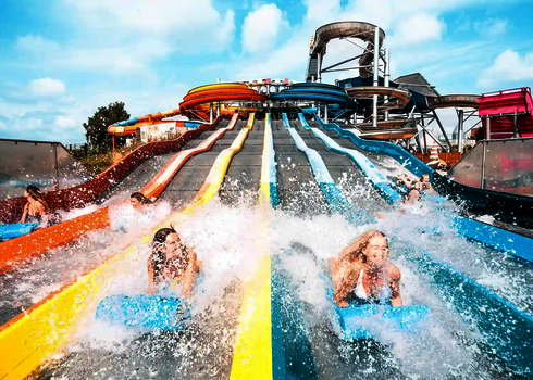 Personen kommen lachend auf Rutschmatten am unteren Ende des Matracers an, Wasser spritzt.