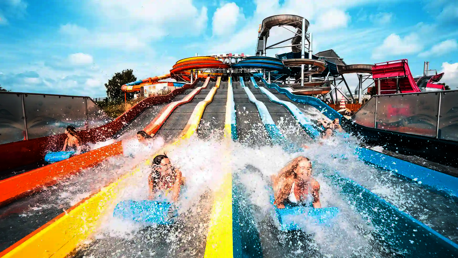 Personen kommen lachend auf Rutschmatten am unteren Ende des Matracers an, Wasser spritzt.