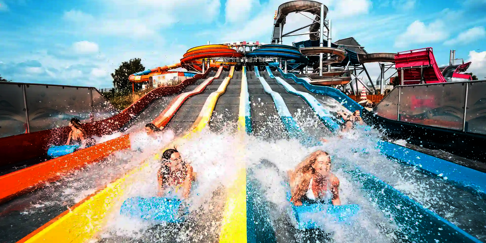 Personen kommen lachend auf Rutschmatten am unteren Ende des Matracers an, Wasser spritzt.