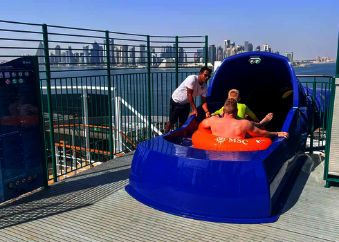 Blauer Startbereich einer Wasserrutsche mit zwei Personen im Reifen und Mann, der daneben steht.