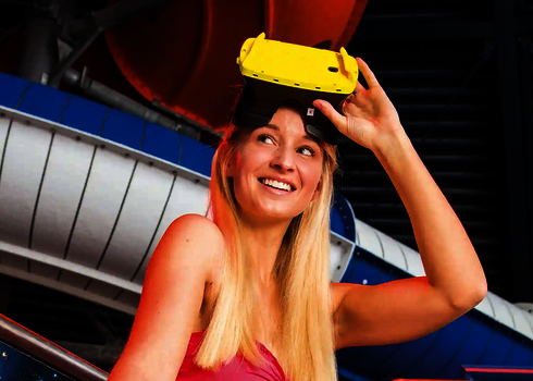 Eine blonde Frau hält lächelnd eine gelbe Virtual Reality Brille für Wasserrutschen in der Hand.