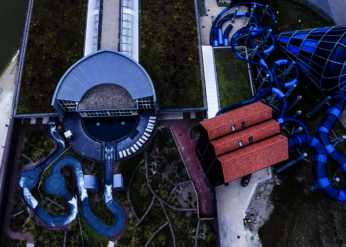 Gesamtübersicht des Freizeitbads mit Wildwasserfluss und blauen Röhrenrutschen von oben.