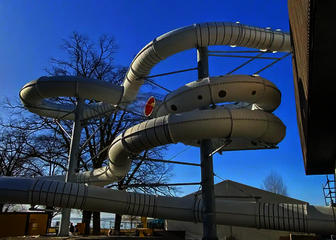 Lange weiße Wasserrutsche, die unter freiem Himmel in ein Gebäude führt.