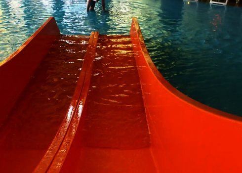 Orangefarbene Multislide Kinderwasserrutsche, die in ein Becken führt.