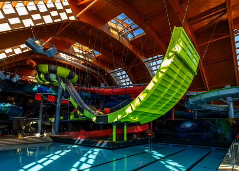 Indoor-Wasserpark mit auffälliger, leuchtend gelber Rampe der Boomerang-Rutsche über Pool.
