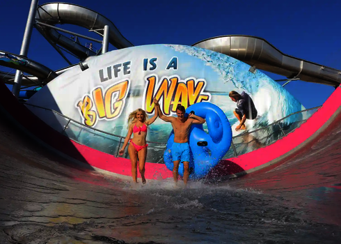 Ein Paar läuft mit einem Reifen aus der Sidewinder vor großem Wellenmotiv.