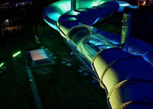 Beleuchtete Family Twister Wasserrutsche bei Nacht mit transparenten Rutschenelementen.