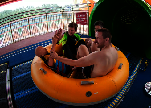 Drei junge Erwachsene sitzen im Rutschreifen, bereit für die Abfahrt durch die Röhre.