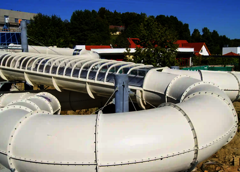 Weiße GFK Wasserrutsche vor Häusern und Bäumen.