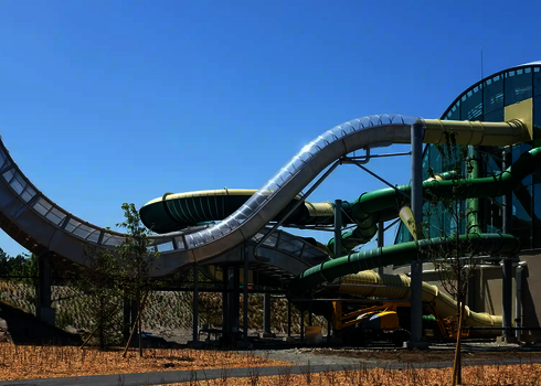 Außenansicht der Boomerang-Rutsche mit transparenter Überdachung und grünem Röhrensystem.