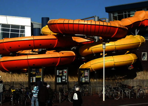 Mehrfarbige Family Twister Reifenrutschen neben einem Schwimmbad und Fahrradständern im Außenbereich.