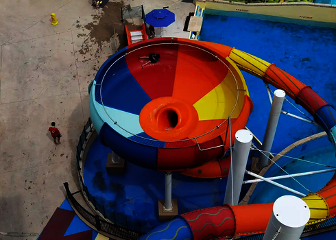 Vogelperspektive einer bunten Body Bowl Wasserrutsche in der eine Person in Badebekleidung rutscht.