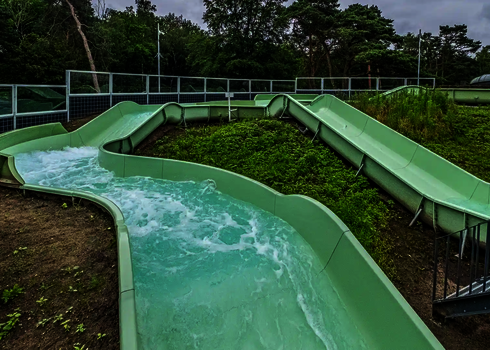 Grüner Wildwasserfluss schlängelt sich durch bepflanzte Hügellandschaft im Außenbereich.