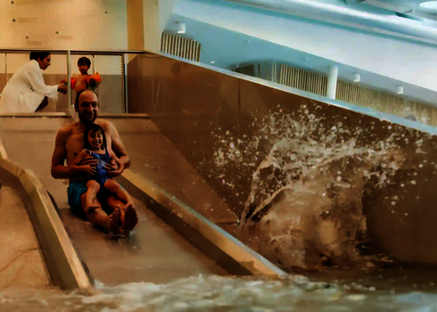 Ein Vater rutscht mit Kind auf der Trio-Slide, nebenan rutscht ein weiteres Kind allein.