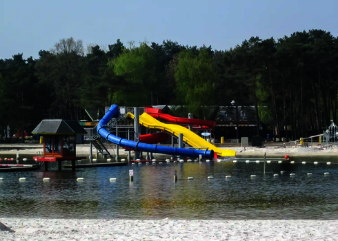  Rutschen in Blau, Gelb und Rot stehen am Ufer eines Naturbadesees mit Sandstrand.
