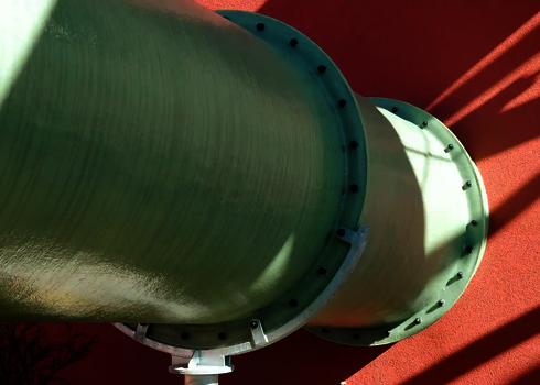 Grüne Wasserrutsche durchquert die rote Gebäudefassade und wird seitlich gestützt.