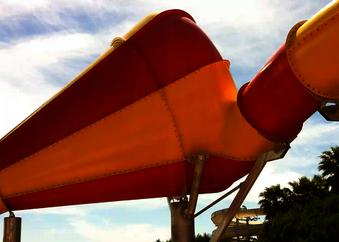 Gelb-rote Crazy Cone Rutsche in Seitenansicht vor Palmen und Himmel.
