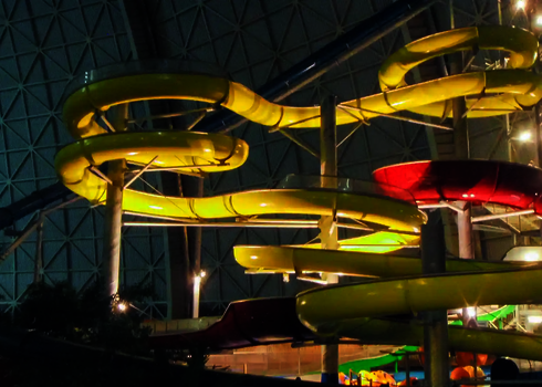 Lange gele Wasserrutsche und roter Crazy River, beides beleuchtet, in abgedunkelter Halle.