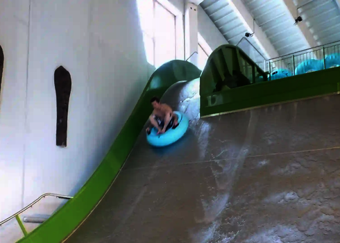 Junge fährt mit Reifen eine grüne Sidewinder im Hallenbad hinunter.