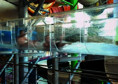 Zwei Personen rutschen gleichzeitig durch ein transparentes Acryl-Stück mit Wasserwirbel-Effekt.