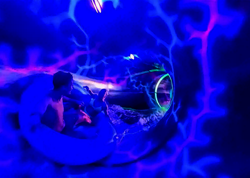 Zwei Personen gleiten in einem Reifen durch eine Wasserrutsche mit leuchtenden UV-Licht und Wie-Glow.
