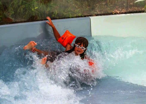 Ein Kind mit Schwimmflügeln und Schwimmbrille landet im Wasser des Wildwasserflusses.