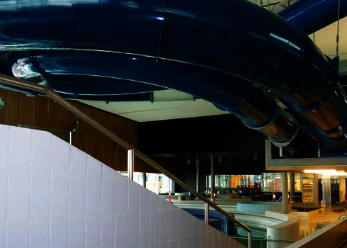 Blick von unten auf eine blaue Wasserrutsche, die von Stahlseilen getragen wird.